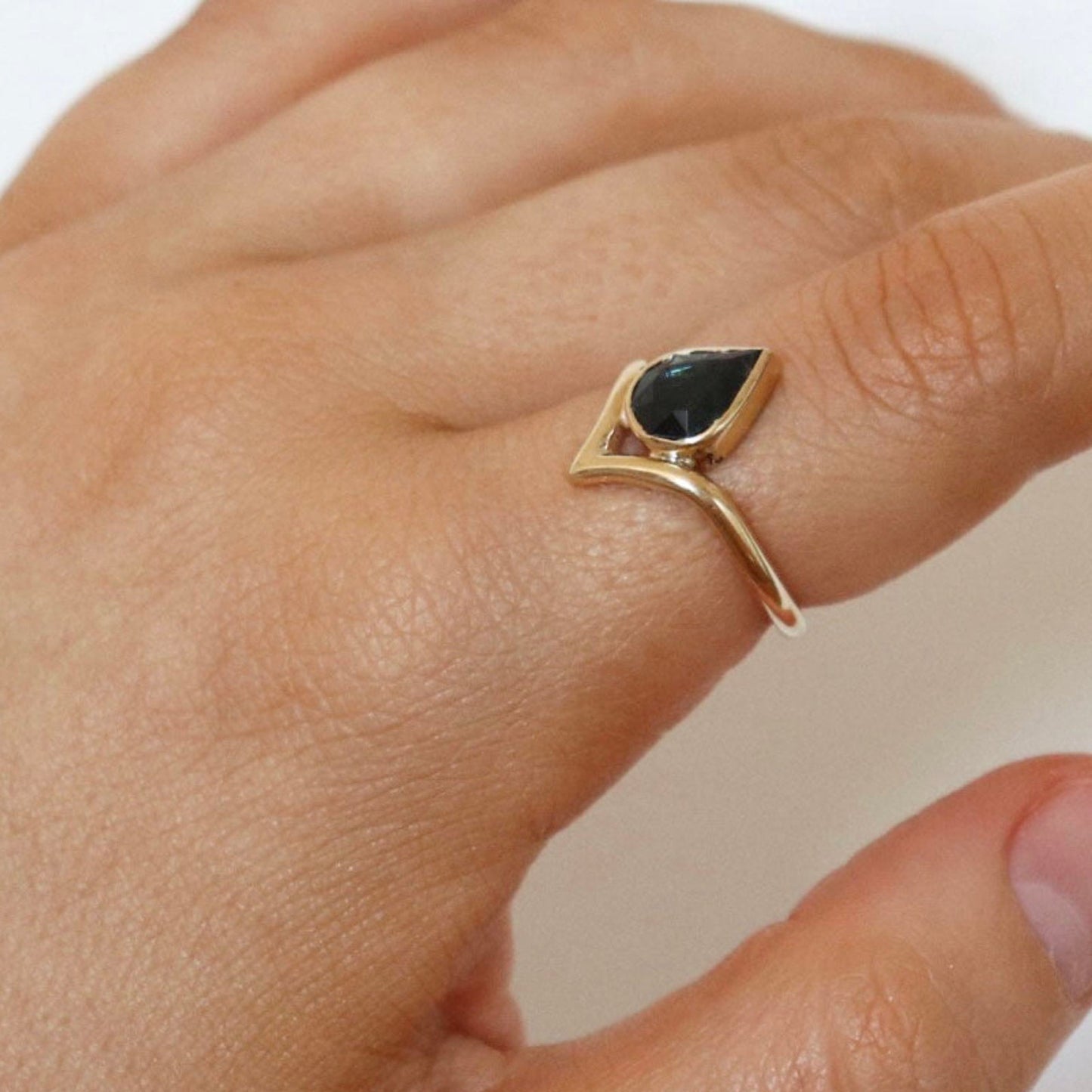 Gold ring with a black gemstone on a hand against a white background
