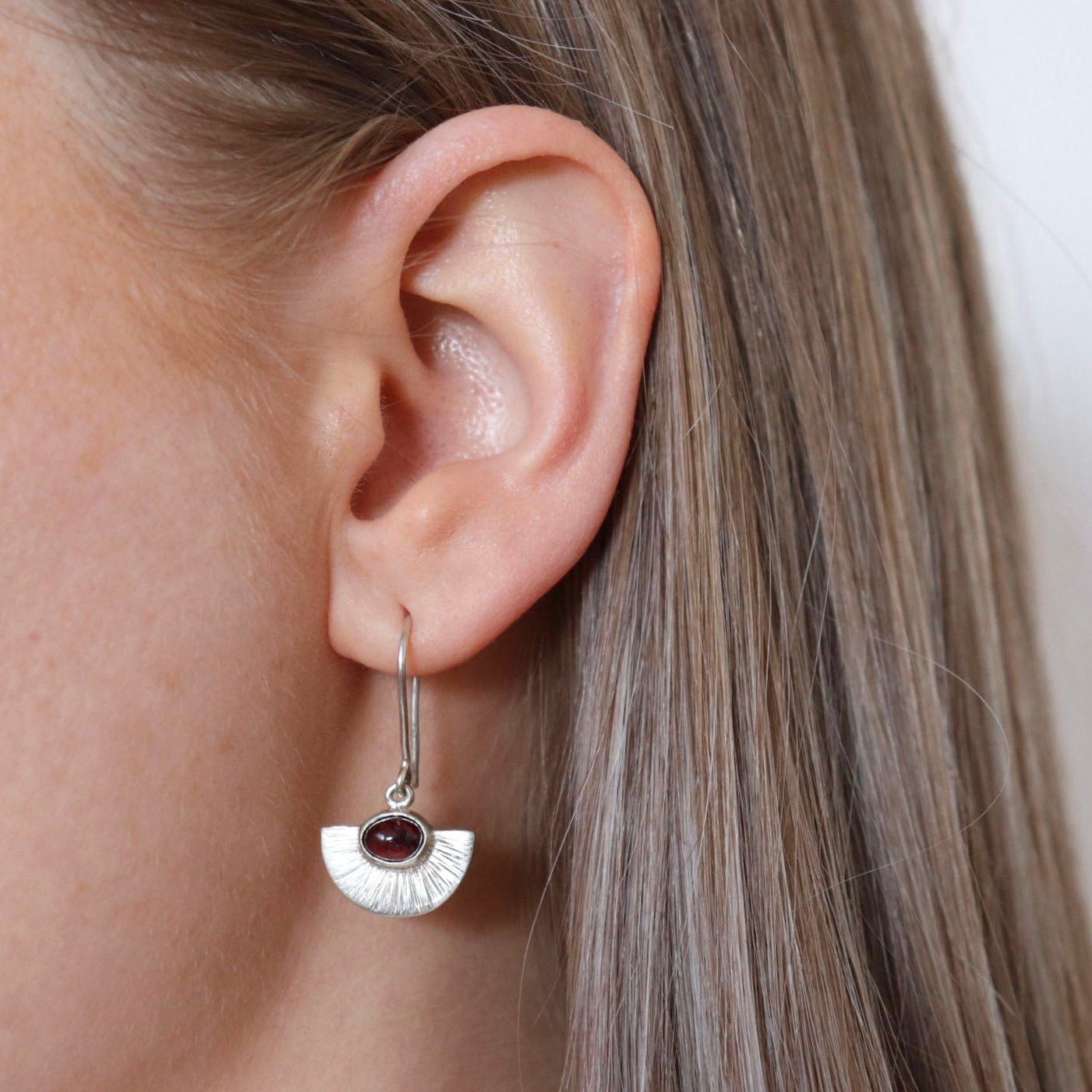 Silver earring with a gemstone worn by a person with light brown hair.